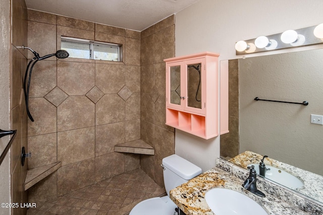 bathroom with a tile shower, vanity, and toilet