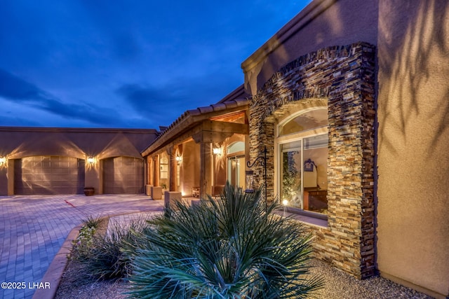 view of side of property featuring a garage, stone siding, decorative driveway, and stucco siding