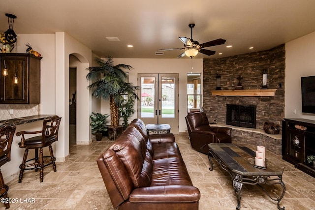 living area with arched walkways, stone tile flooring, a fireplace, and french doors