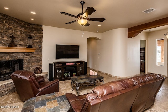 living area featuring arched walkways, a stone fireplace, stone tile floors, a ceiling fan, and visible vents