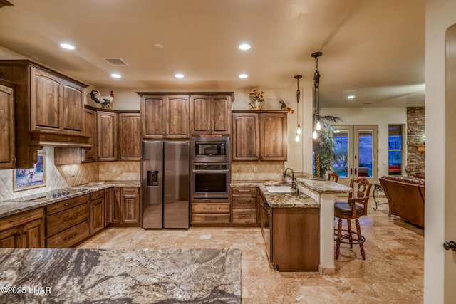 kitchen featuring a peninsula, a sink, visible vents, a kitchen breakfast bar, and appliances with stainless steel finishes