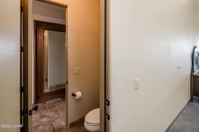 bathroom with stone finish flooring, baseboards, and toilet