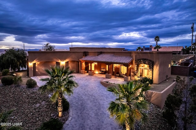 back of property at dusk featuring decorative driveway and an attached garage