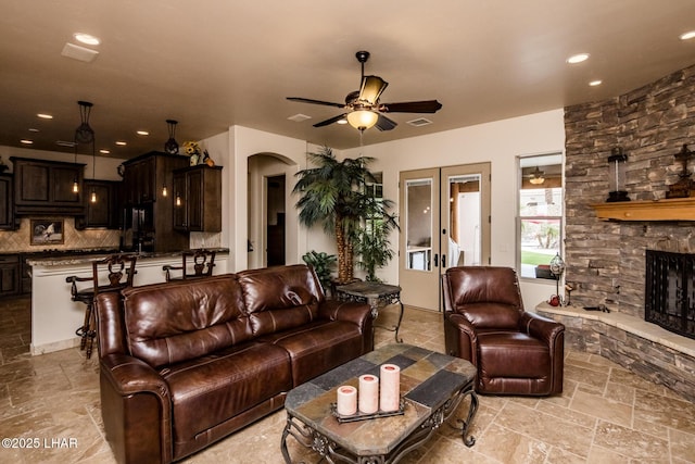 living area featuring stone tile floors, arched walkways, a ceiling fan, a fireplace, and recessed lighting