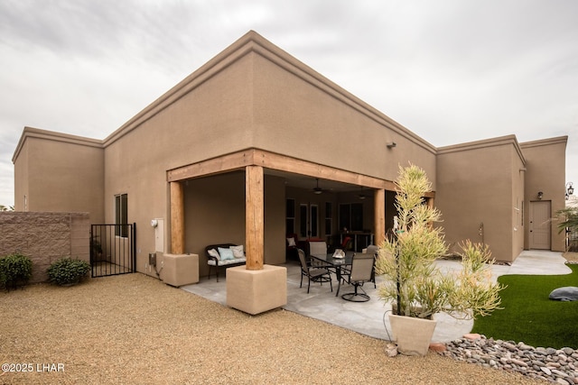 rear view of property with ceiling fan, a patio area, a gate, and stucco siding