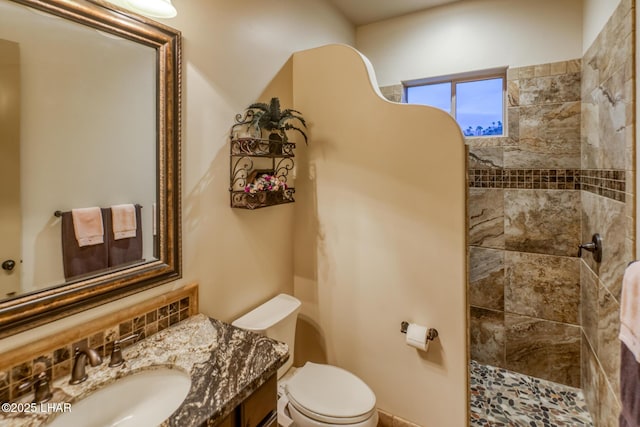 bathroom featuring vanity, tiled shower, backsplash, and toilet