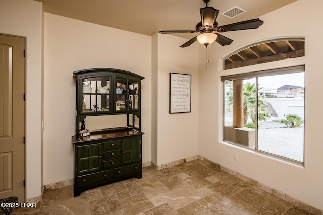 interior space featuring baseboards, a ceiling fan, visible vents, and stone tile floors