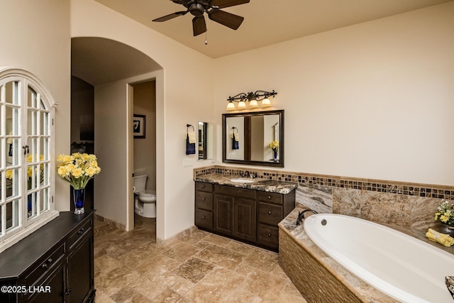 bathroom featuring a ceiling fan, vanity, toilet, and a bath