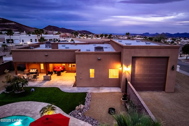 back of property at dusk featuring stucco siding, a mountain view, an attached garage, and a patio