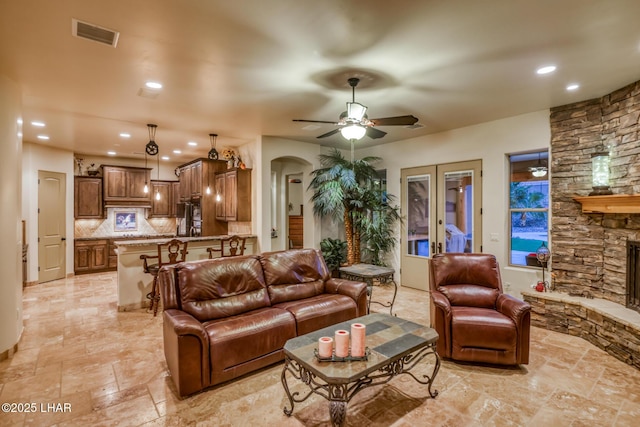 living room featuring arched walkways, recessed lighting, visible vents, ceiling fan, and a stone fireplace