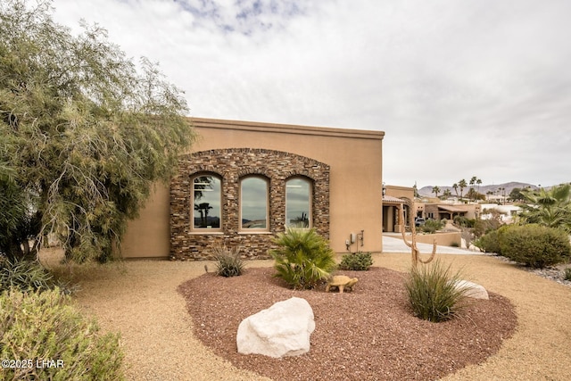 view of front facade with stone siding, a patio, and stucco siding