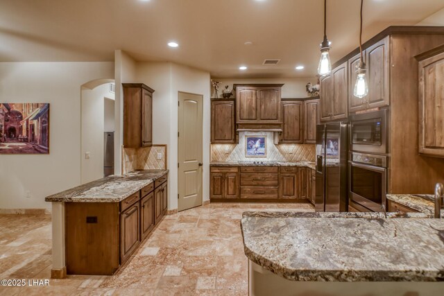 kitchen with arched walkways, decorative backsplash, appliances with stainless steel finishes, light stone counters, and a peninsula