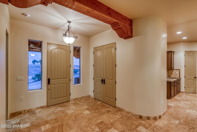 foyer entrance featuring stone finish floor, visible vents, beamed ceiling, and baseboards