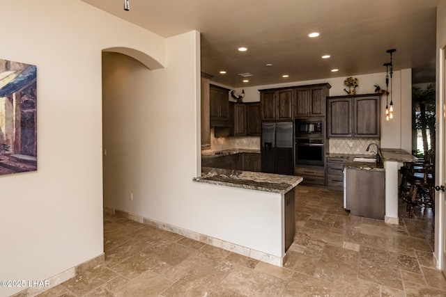 kitchen with dark stone countertops, a peninsula, dark brown cabinets, black appliances, and a sink