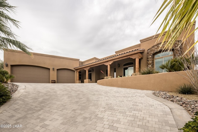 view of front facade featuring a tiled roof, decorative driveway, an attached garage, and stucco siding