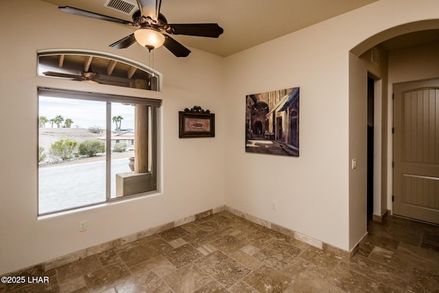 empty room featuring baseboards, visible vents, arched walkways, ceiling fan, and stone finish floor