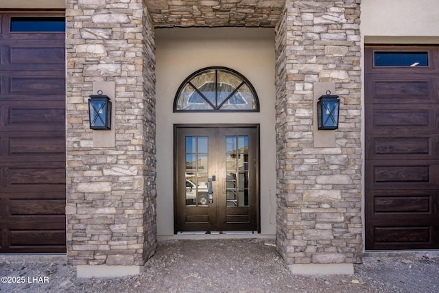 entrance to property featuring a garage, stone siding, french doors, and stucco siding