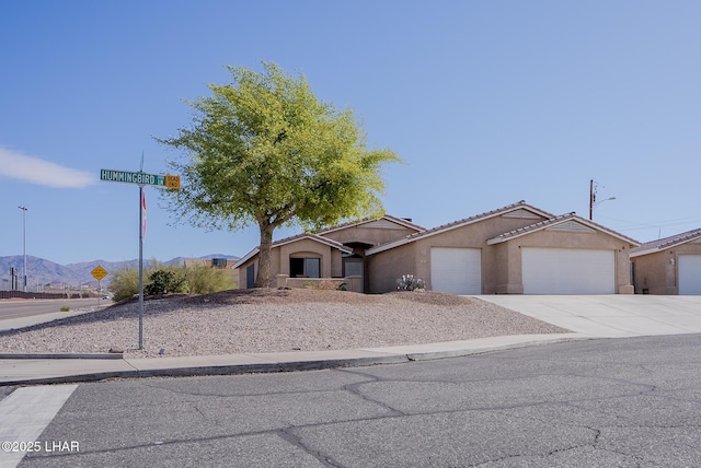 view of front of home featuring a tiled roof, concrete driveway, stucco siding, a garage, and a mountain view