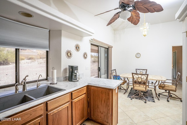 kitchen with light countertops, light tile patterned floors, brown cabinets, a peninsula, and a sink