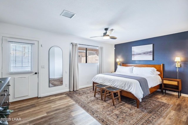 bedroom featuring baseboards, wood finished floors, visible vents, and ceiling fan
