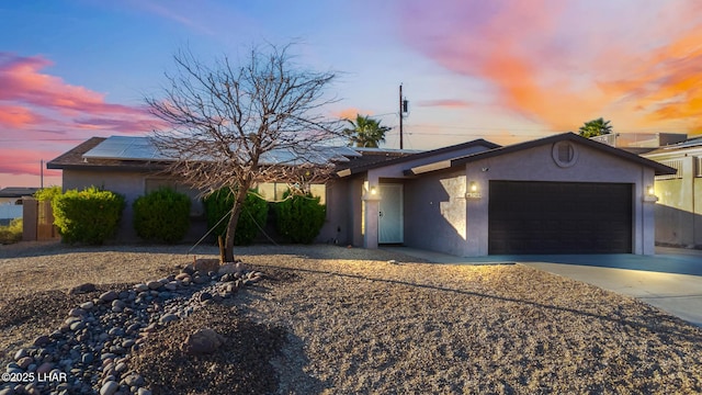 ranch-style house with roof mounted solar panels, an attached garage, stucco siding, and driveway