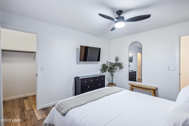 bedroom featuring arched walkways, baseboards, wood finished floors, a closet, and a walk in closet