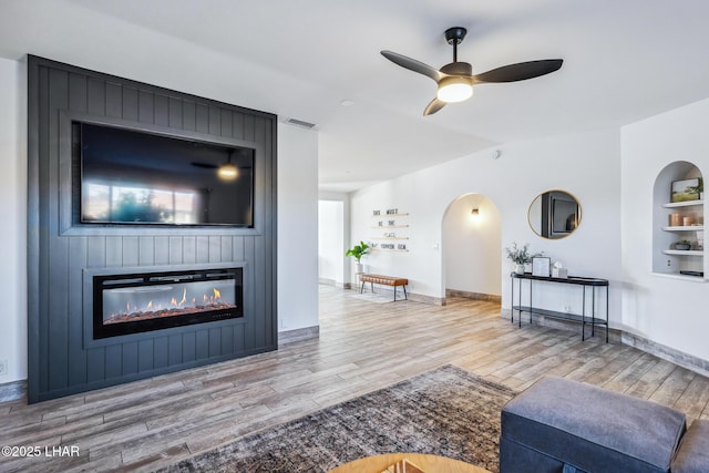 living area with wood finished floors, visible vents, baseboards, a large fireplace, and ceiling fan