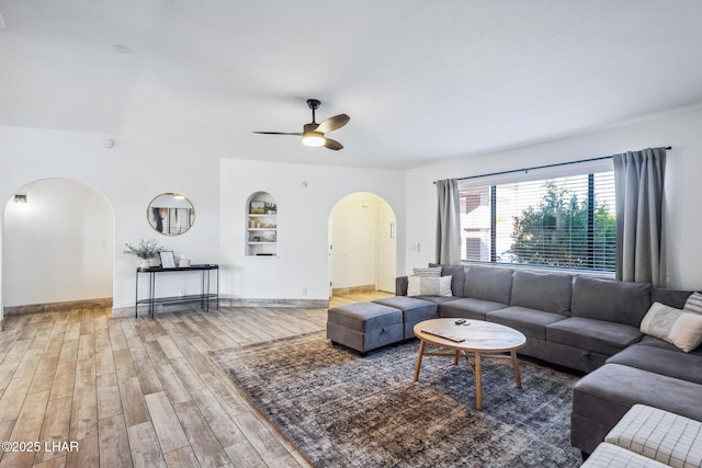 living area with ceiling fan, arched walkways, built in features, and wood finished floors
