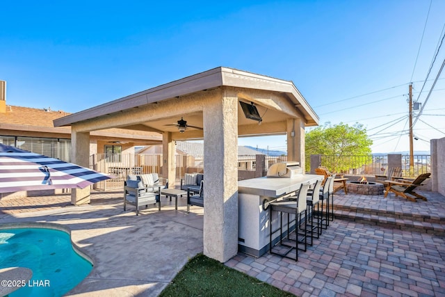 view of patio / terrace featuring a ceiling fan, a fire pit, outdoor dry bar, fence, and a fenced in pool