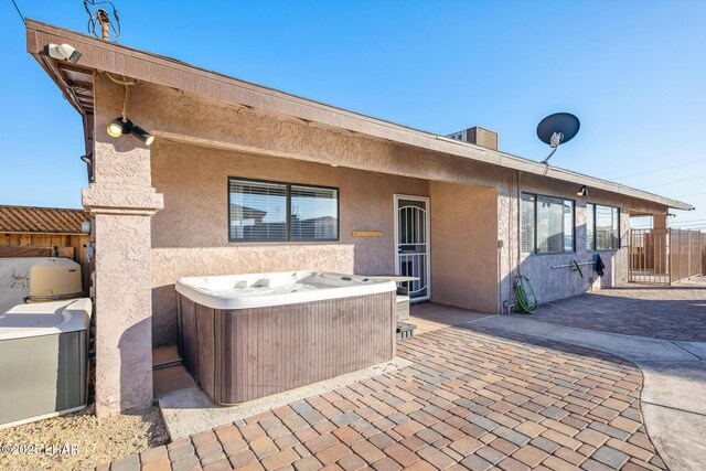 back of house with fence, a patio area, a hot tub, and stucco siding