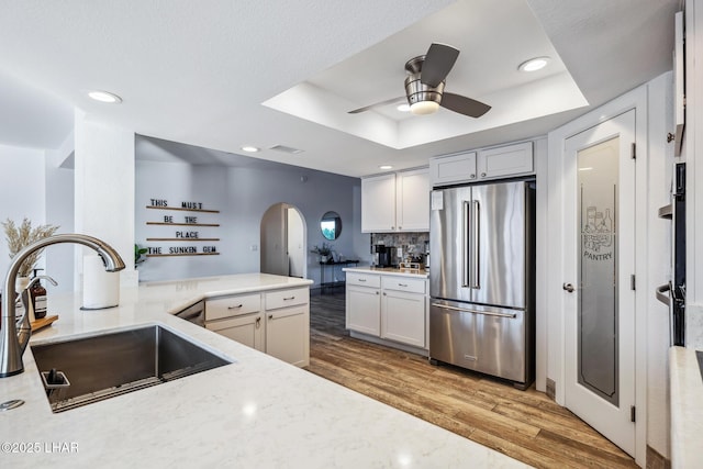 kitchen featuring a ceiling fan, high end fridge, a sink, arched walkways, and a tray ceiling