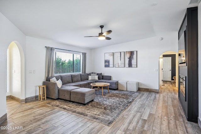 living room featuring ceiling fan, arched walkways, light wood-style floors, and baseboards