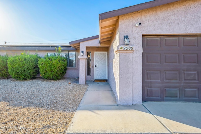 doorway to property featuring an attached garage and stucco siding