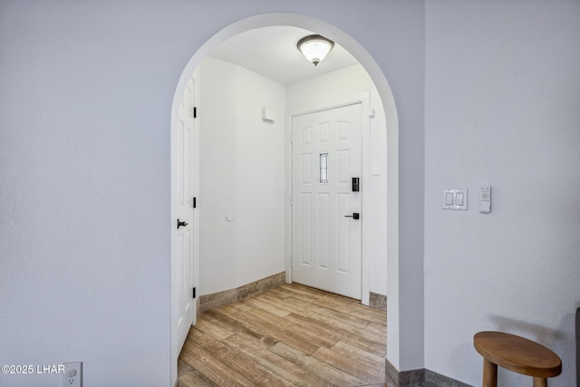 foyer featuring light wood-type flooring, baseboards, and arched walkways