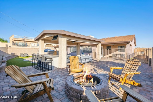 view of patio featuring ceiling fan, a fenced backyard, a fire pit, and an outdoor bar