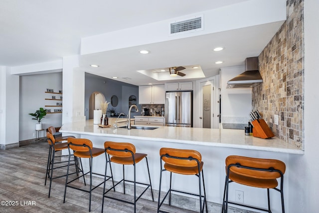 kitchen with stainless steel fridge, a sink, visible vents, decorative backsplash, and wall chimney range hood