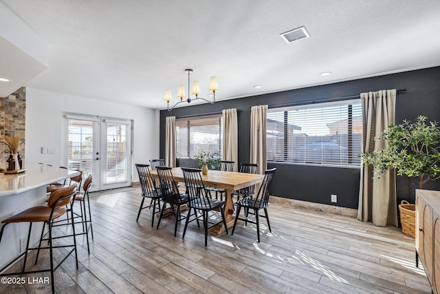 dining space with a chandelier, french doors, visible vents, and light wood-style floors