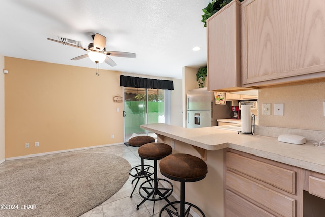 kitchen with stainless steel refrigerator with ice dispenser, a breakfast bar, light brown cabinets, and light tile patterned floors