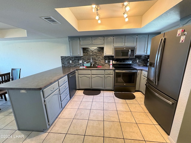 kitchen featuring kitchen peninsula, light tile patterned floors, stainless steel appliances, and a raised ceiling