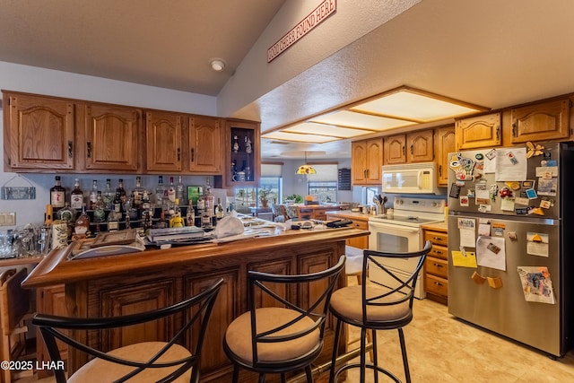 kitchen with a kitchen bar, lofted ceiling, a peninsula, brown cabinetry, and white appliances