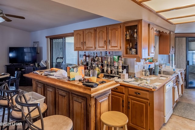 kitchen with brown cabinetry, ceiling fan, light countertops, glass insert cabinets, and dishwasher