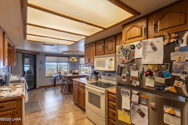 kitchen with visible vents, baseboards, pendant lighting, brown cabinetry, and white appliances