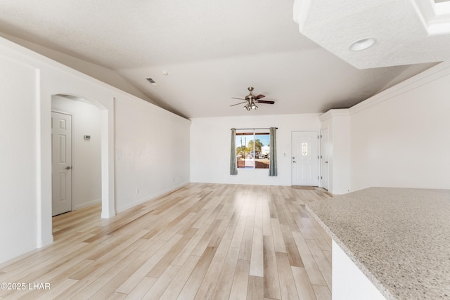 unfurnished living room with lofted ceiling, light wood-style flooring, arched walkways, and ceiling fan