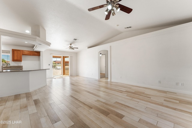 unfurnished living room featuring a ceiling fan, arched walkways, visible vents, and light wood-style flooring