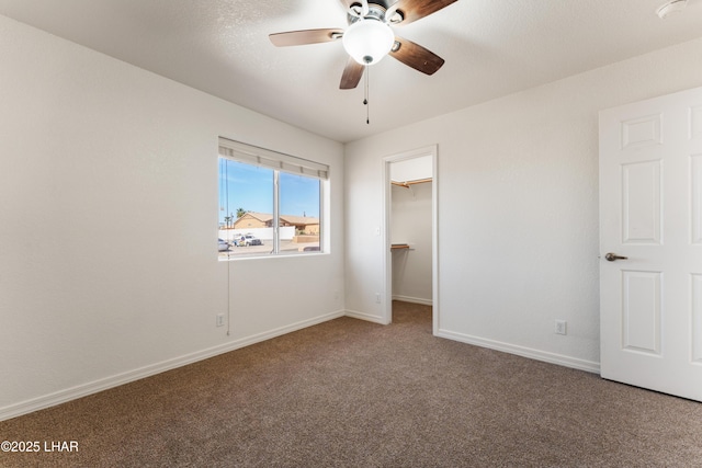 unfurnished bedroom with a ceiling fan, baseboards, a spacious closet, a closet, and carpet