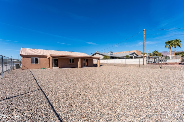 rear view of house featuring a fenced backyard, a tile roof, and stucco siding