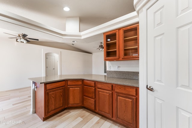 kitchen featuring light wood-style flooring, recessed lighting, a peninsula, brown cabinetry, and glass insert cabinets