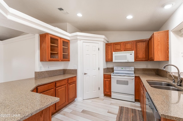 kitchen featuring light wood finished floors, visible vents, brown cabinetry, a sink, and white appliances