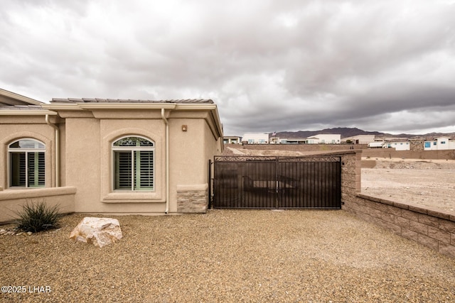 view of side of home featuring stucco siding, a tiled roof, and a gate