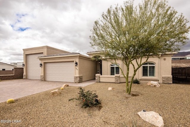 view of front facade featuring decorative driveway, fence, a garage, and stucco siding